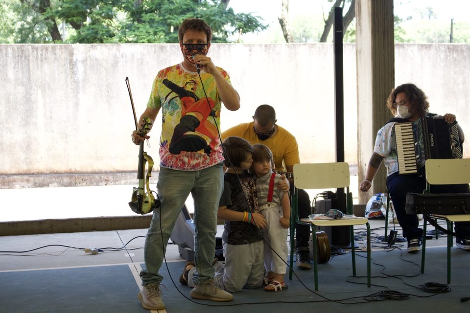 Roney Marczak segura o violino perto de duas crianças agachadas.