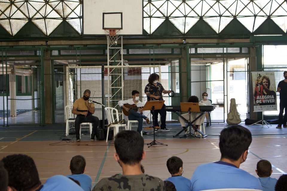 O grupo toca sob a tabela de basquete, visto por trás da plateia.