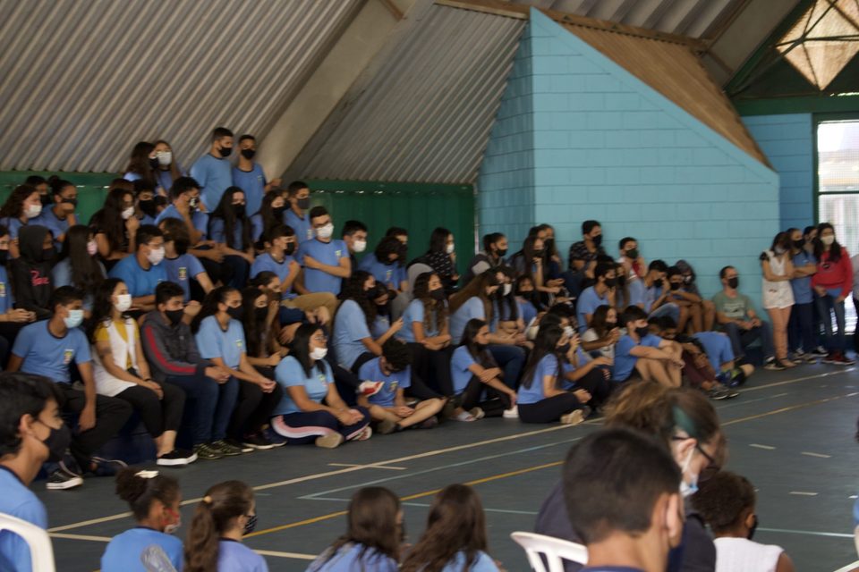 Arquibancada lotada de estudantes de uniforme azul, de máscara.