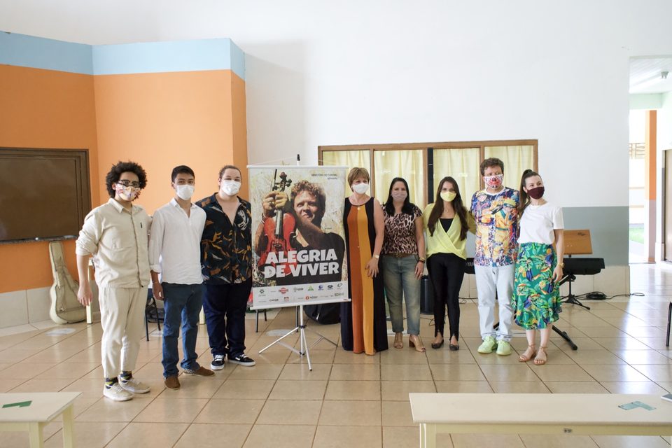 Músicos e equipe da escola posam ao lado do banner do disco.