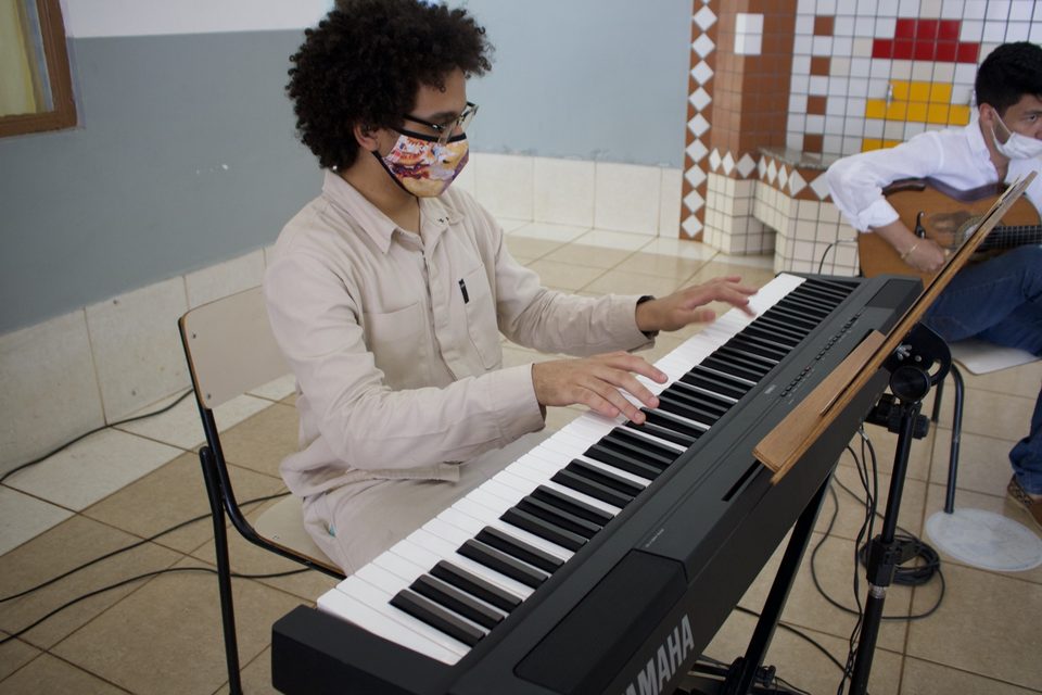 Um jovem músico de camisa clara toca teclado.