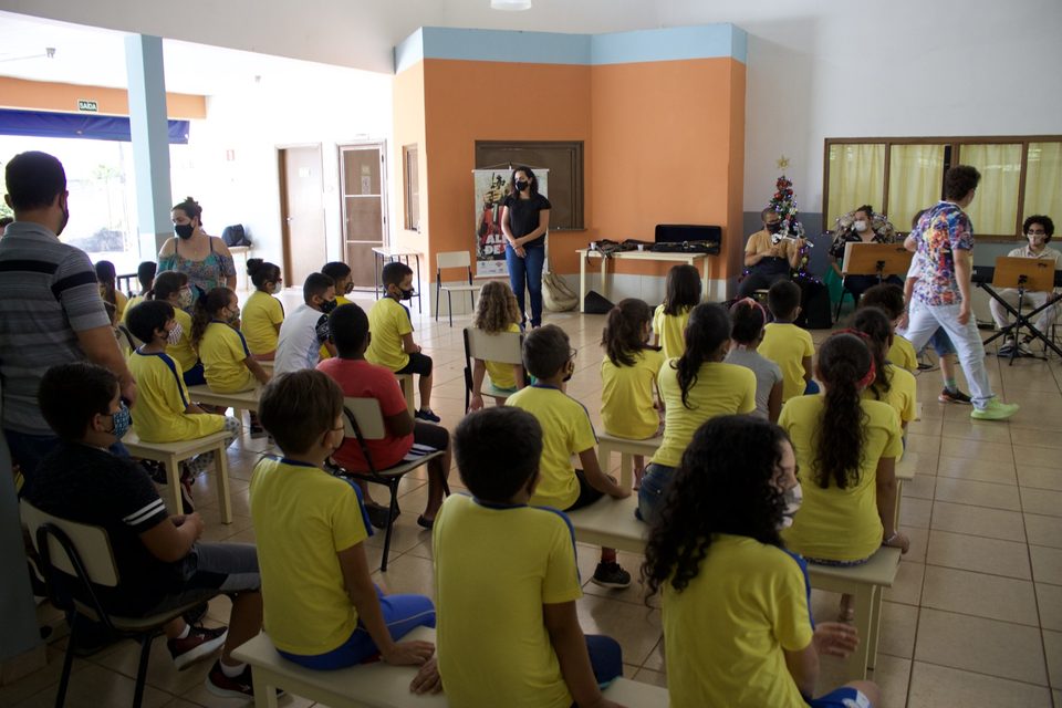 As crianças assistem de perto ao grupo, que toca ao fundo do salão.
