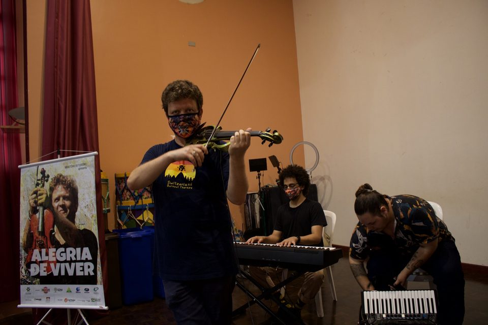 Roney Marczak toca violino no palco, com o teclado ao fundo.