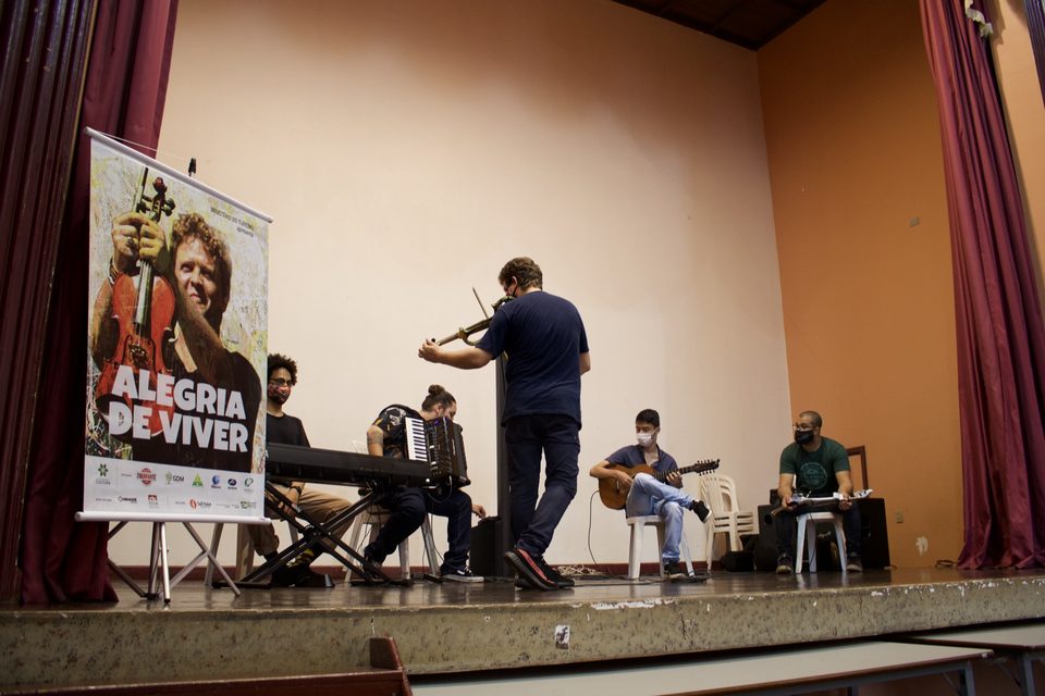 O grupo no palco do auditório, ao lado do banner do disco.