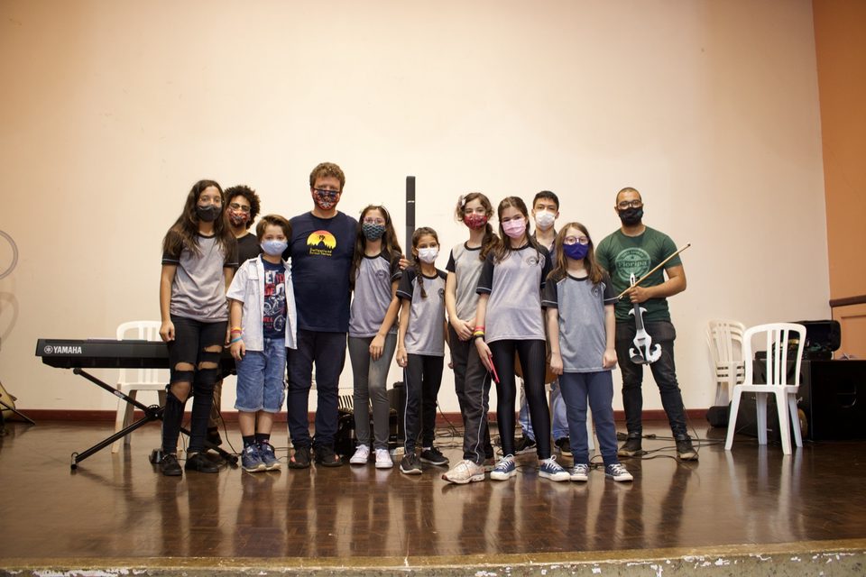 Músicos e estudantes posam juntos no palco.