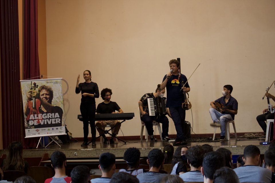 Uma mulher gesticula na beira do palco enquanto o grupo toca.