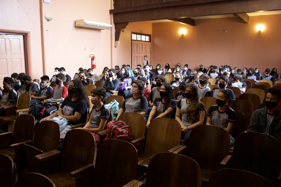 Estudantes assistem das poltronas do auditório.