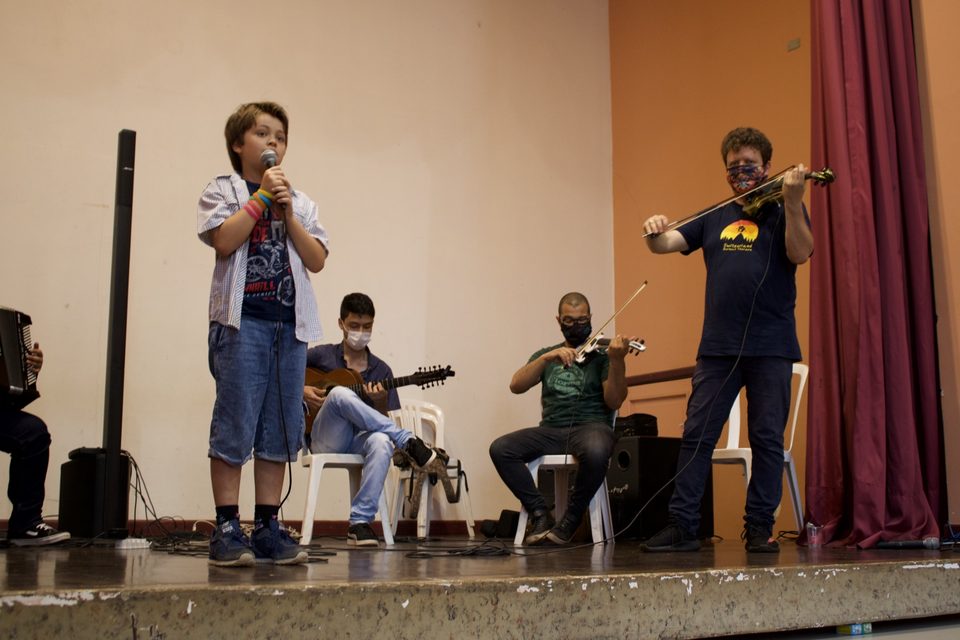 O menino canta de um lado do palco; Roney Marczak toca do outro.