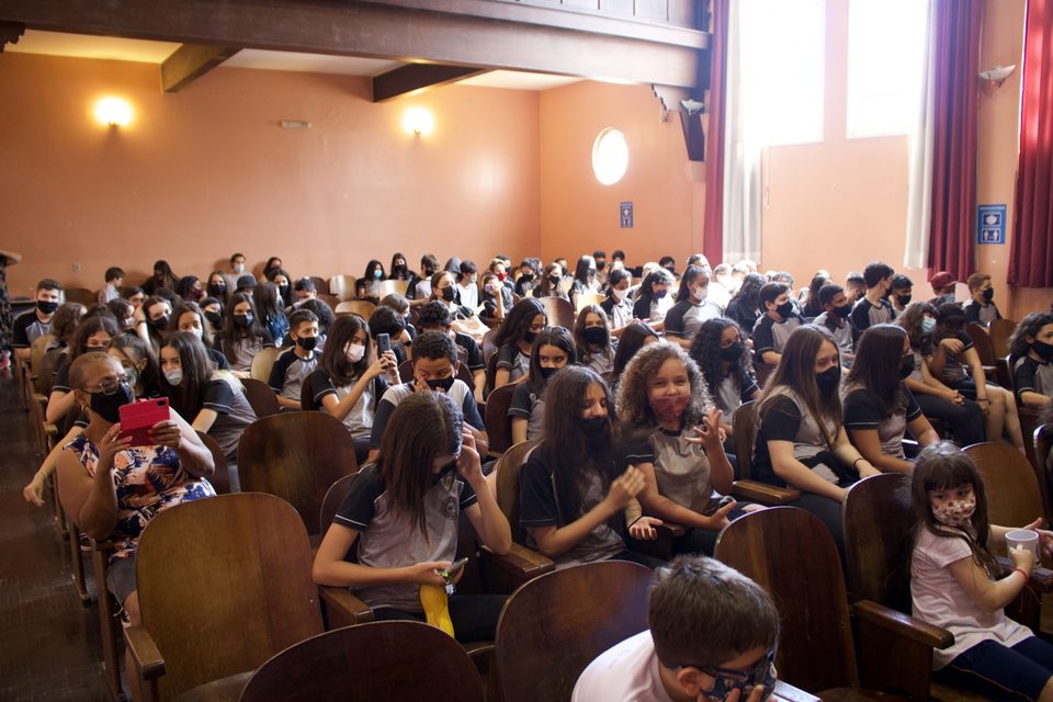 Estudantes nas poltronas do auditório, de máscara.