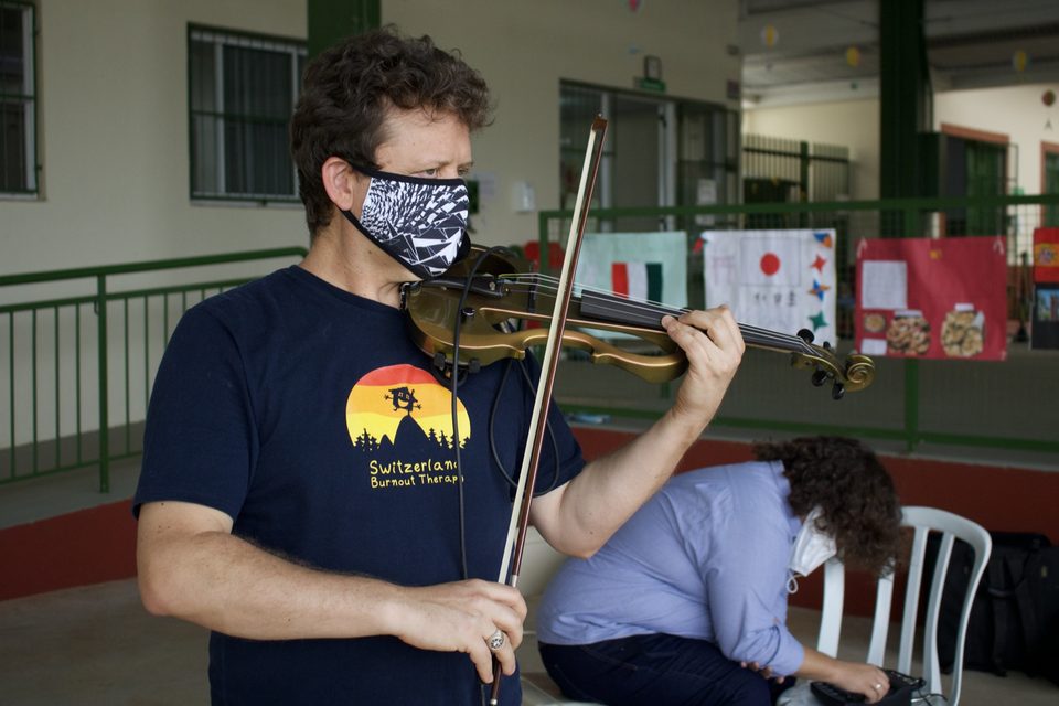Roney Marczak, de máscara, toca violino em primeiro plano.