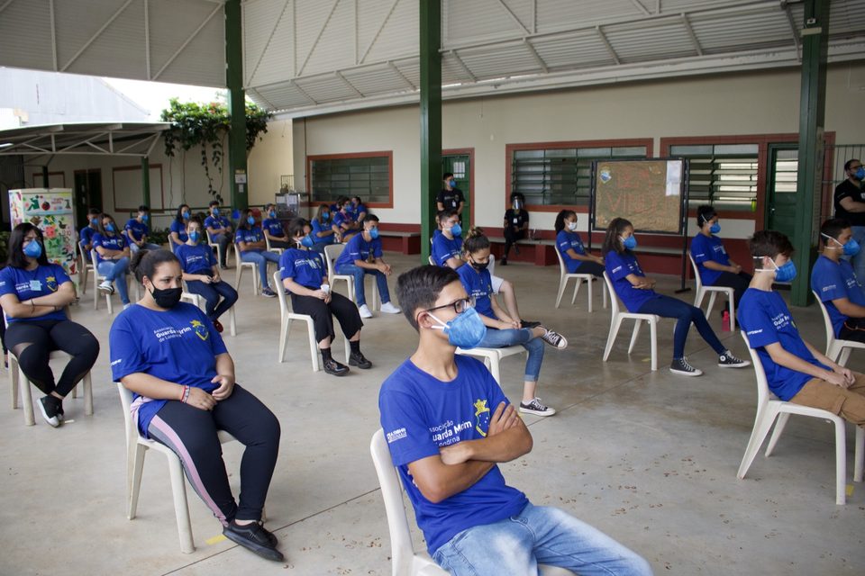 Plateia de jovens de camiseta azul, sentados em cadeiras brancas.