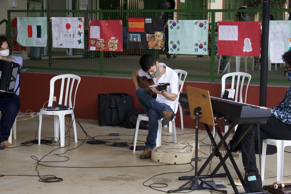 Um jovem toca violão sentado; ao lado, o teclado.
