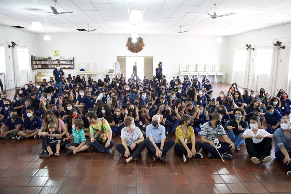 Centenas de estudantes de uniforme azul-marinho sentados no chão do salão, para a foto com os músicos.