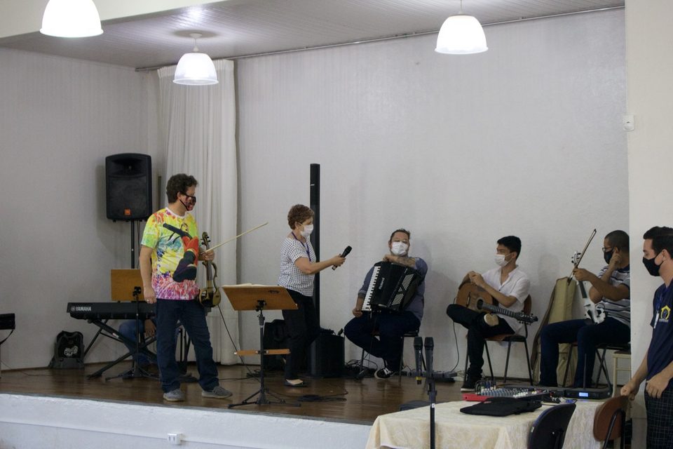 Roney Marczak e os músicos no palco; uma pessoa fala ao microfone.