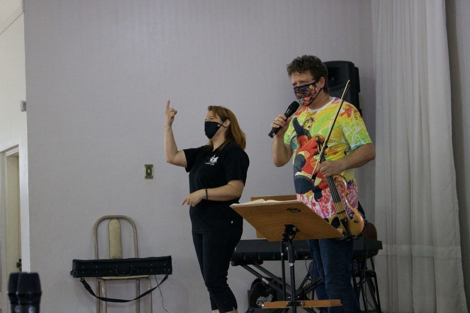 Uma mulher gesticula ao lado de Roney Marczak, que fala ao microfone.