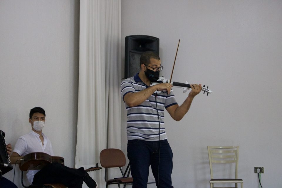 Um músico de camisa listrada toca violino elétrico, de pé.