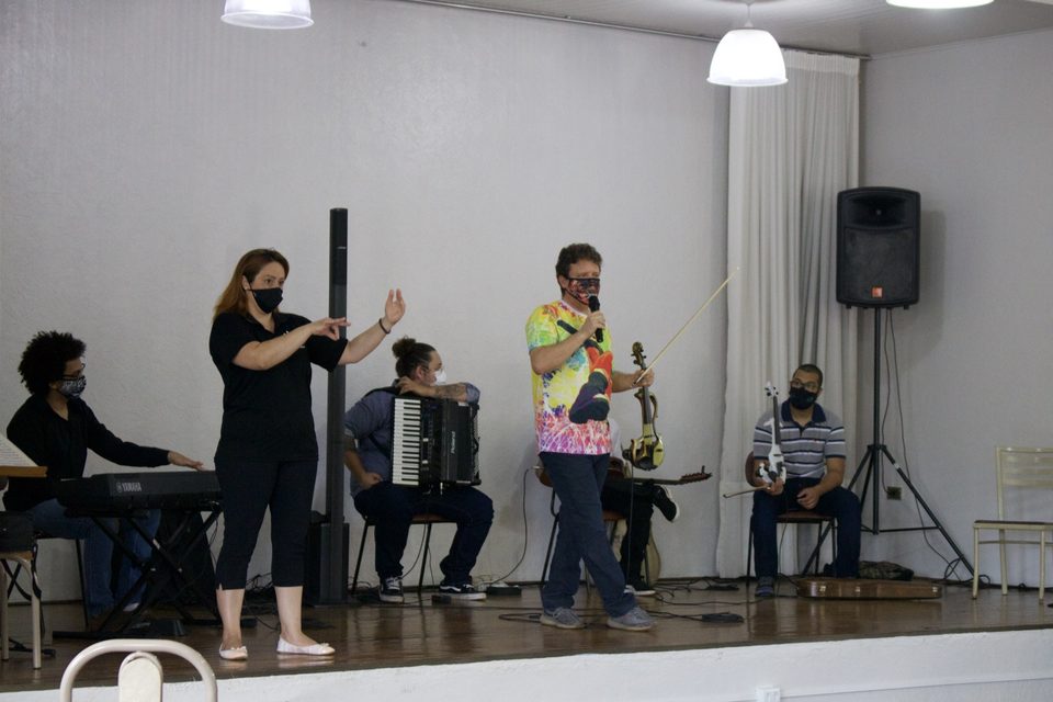 Uma mulher gesticula enquanto o grupo toca no palco.