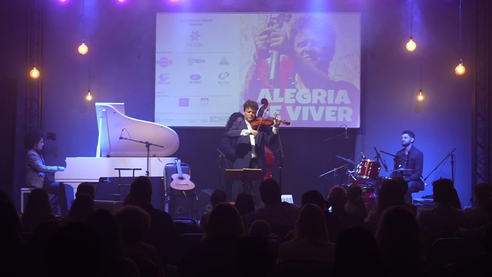 O grupo completo no palco, diante do telão com a capa do disco.