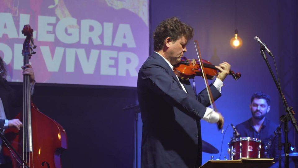 Roney Marczak toca violino diante do telão, entre o contrabaixo e a bateria.