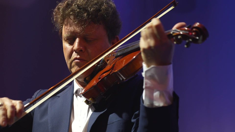 Roney Marczak em primeiro plano, de olhos baixos sobre o violino, com o arco atravessando o quadro.