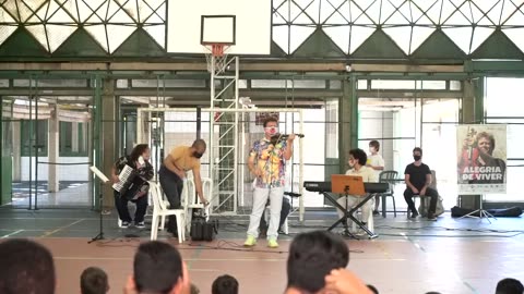 Vídeo: o grupo toca no centro da quadra coberta, diante dos estudantes de uniforme azul.
