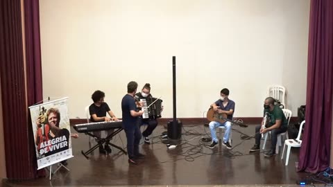 Vídeo: o grupo toca no palco do auditório, ao lado do banner do disco.