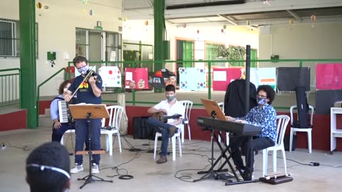 Vídeo: o grupo toca no pátio coberto, com teclado, violão e violino.