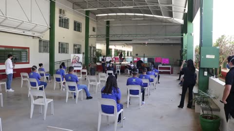 Vídeo: a apresentação vista do fundo do pátio, com os jovens sentados em cadeiras afastadas.