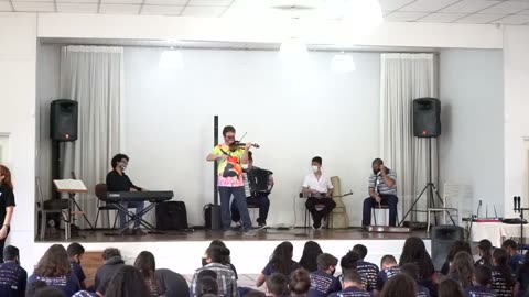 Vídeo: Roney Marczak toca violino ao centro do palco, entre os músicos.